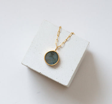 round labradorite pendant on a gold chain draped over the white cube