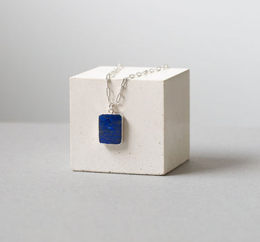 blue rectangular lapiz lazuli pendant on a silver chain draped over the white cube