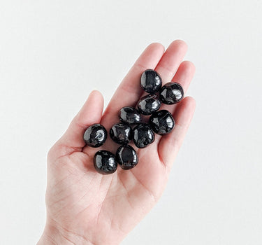 A bunch of dark red, tumbled garnet stones held on an open hand.